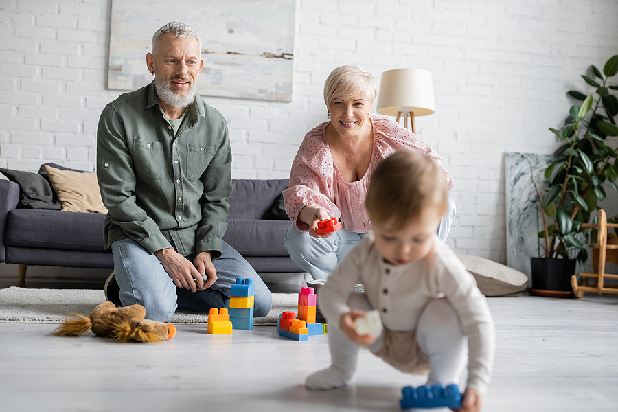 grandparents watching toddler play on the floor with blocks