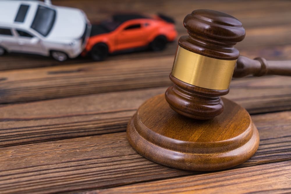 A judge's gavel with two colliding cars in an accident scene, representing traffic accidents, court law, insurance, and fault.
