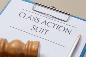 Class action lawsuit document on clipboard with gavel and pen on desk.