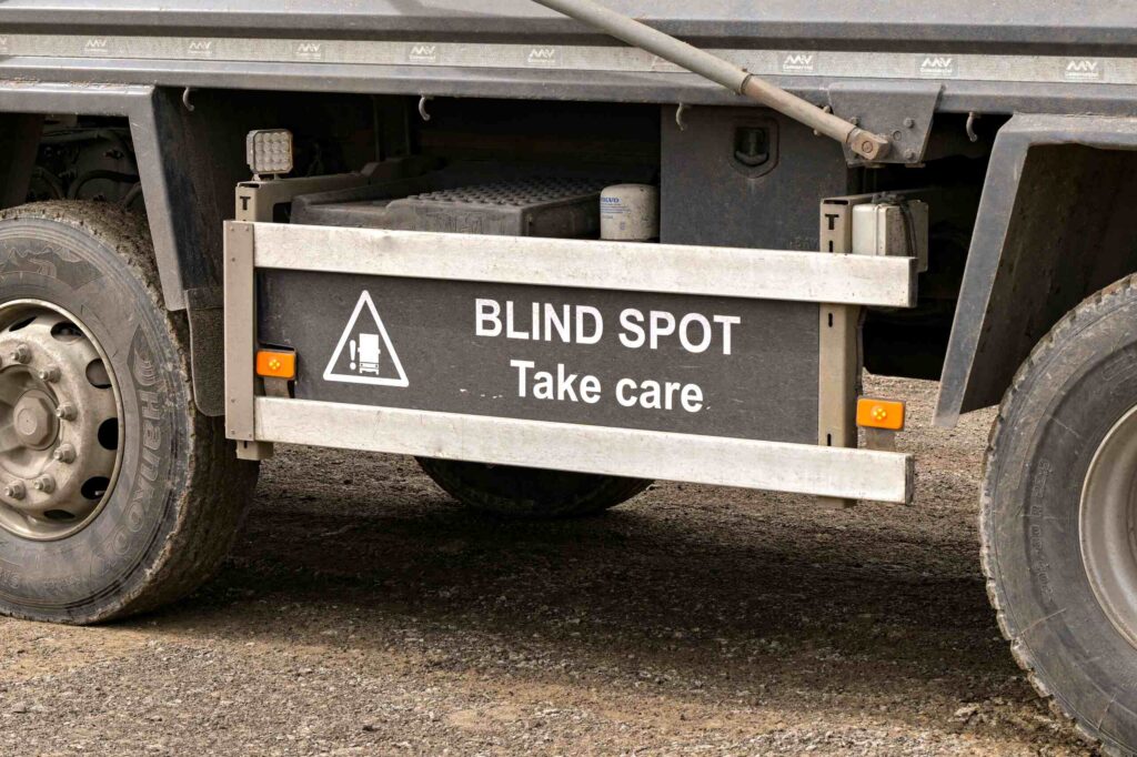 A close-up of a "BLIND SPOT Take care" warning sign on the side of a large commercial truck. Boca Raton truck accident lawyers investigate visibility issues and driver negligence in serious highway collisions.