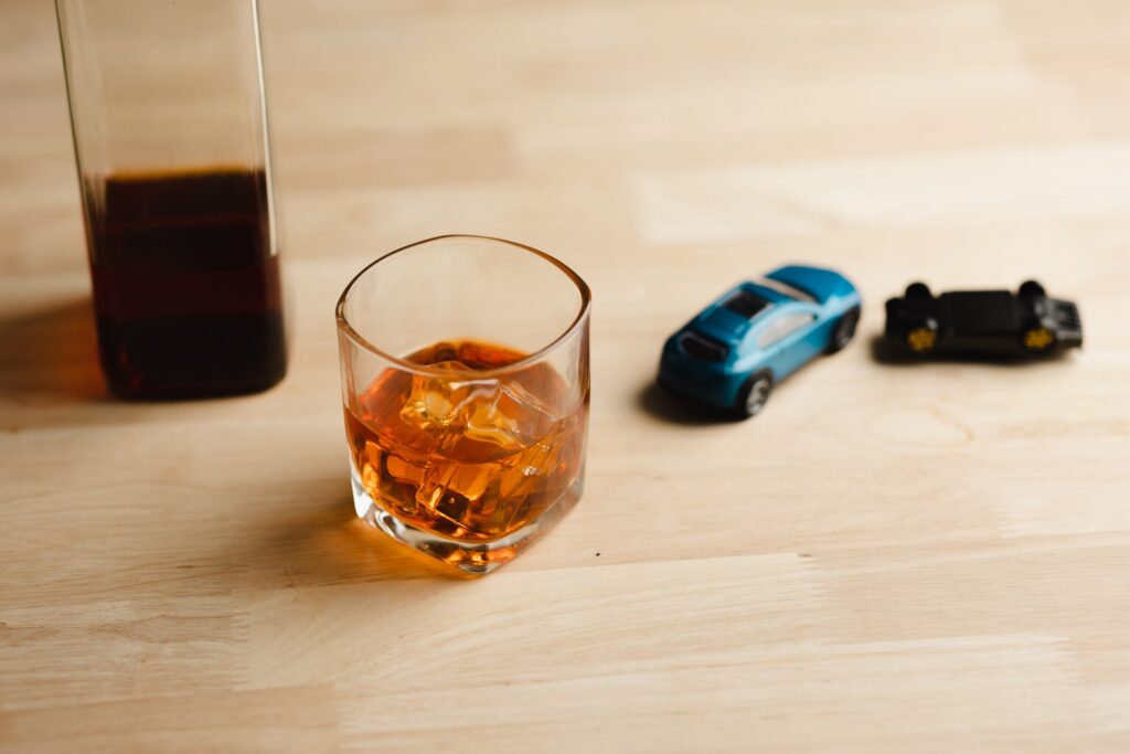 A glass of liquor next to a toy car flipped upside down, illustrating a crash lawsuit represented by Boca Raton Drunk Driving Accident Lawyers.