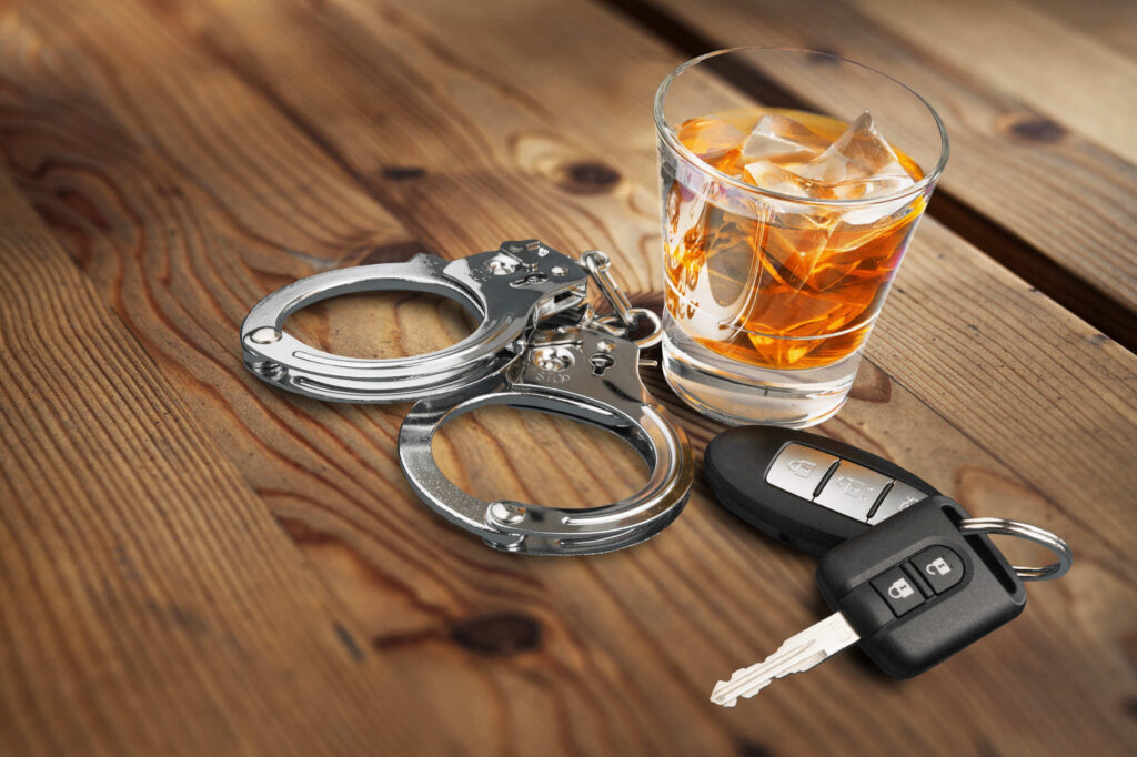 Handcuffs, a car key, and a glass of alcohol on a wooden table, representing cases handled by Boca Raton Drunk Driving Accident Lawyers.