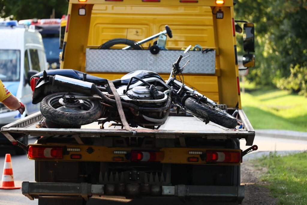 A damaged motorcycle strapped to the back of a flatbed tow truck at a crash scene, illustrating an injury case handled by Boca Raton Motorcycle Accident Lawyers.