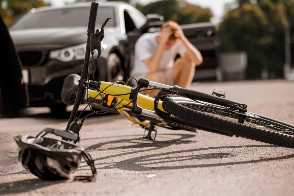 A yellow bicycle and helmet on the ground near an open car door after a collision, highlighting street safety and pedestrian right-of-way laws in Boca Raton.