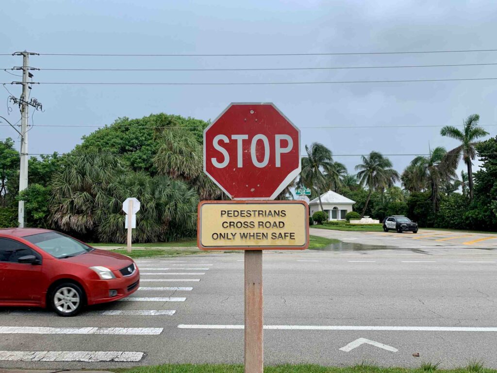 A close-up of an individual using a rolling walker to safely cross a paved street, highlighting pedestrian right-of-way laws in Boca Raton.